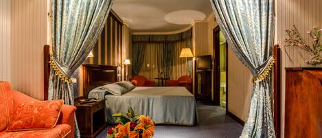 A hotel room with a large bed, a sofa, a nightstand, a lamp, and a vase with flowers.