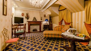 A room with a patterned carpet, a television, a fireplace, a sofa, and a dining table with a tray. - Hotel Infanta Cristina (Jaén)