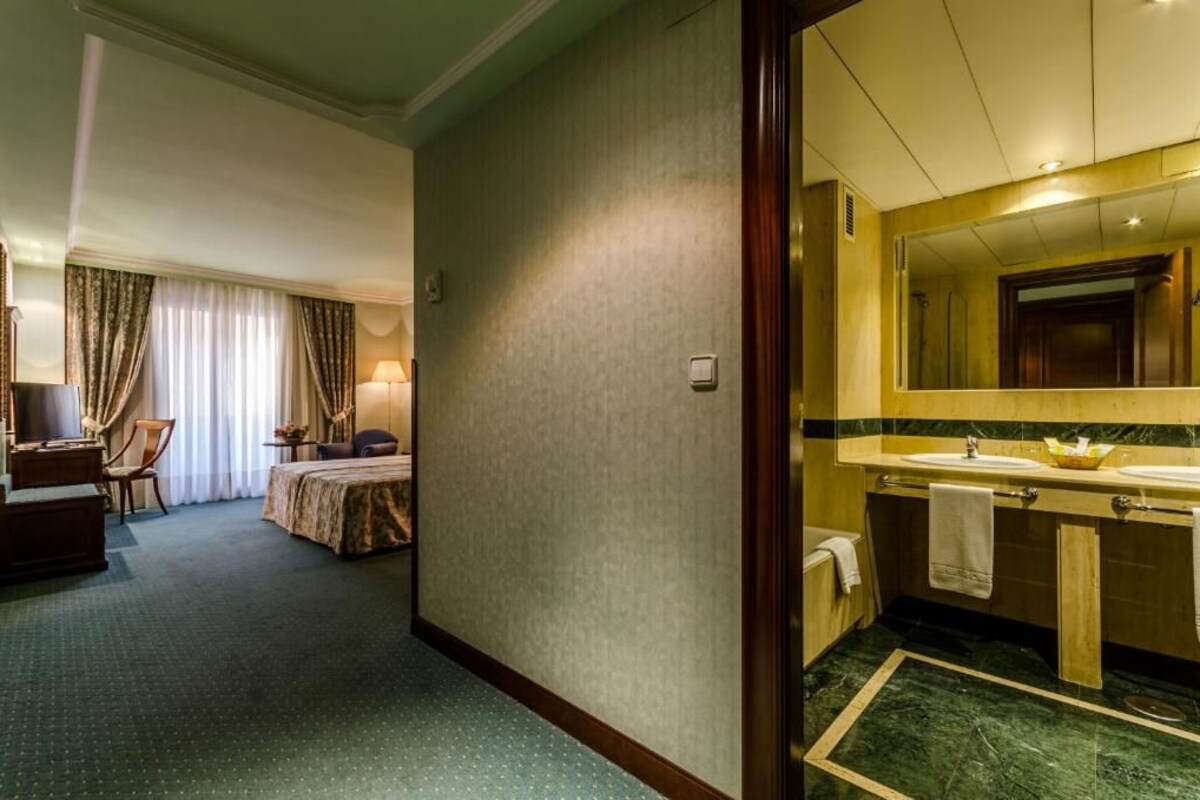 Une chambre d’hôtel comprenant un lit, un bureau, une chaise, une lampe et une salle de bain avec un lavabo et un miroir.