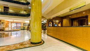 A hotel lobby with a marble floor, a large central column, a reception desk, and a sign for the concierge. - Hotel Infanta Cristina (Jaén)
