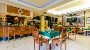 Un bar espacioso con taburetes altos y un suelo de mármol pulido, rodeado de diversas opciones de asiento y un gran árbol decorativo.