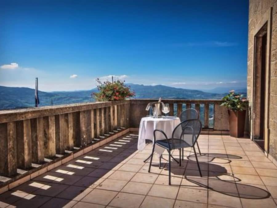 A balcony with a table and chairs, overlooking a mountainous landscape.