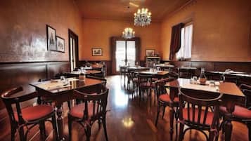 Un restaurante espacioso con mesas y sillas de madera, una araña de cristal y cuadros en las paredes.