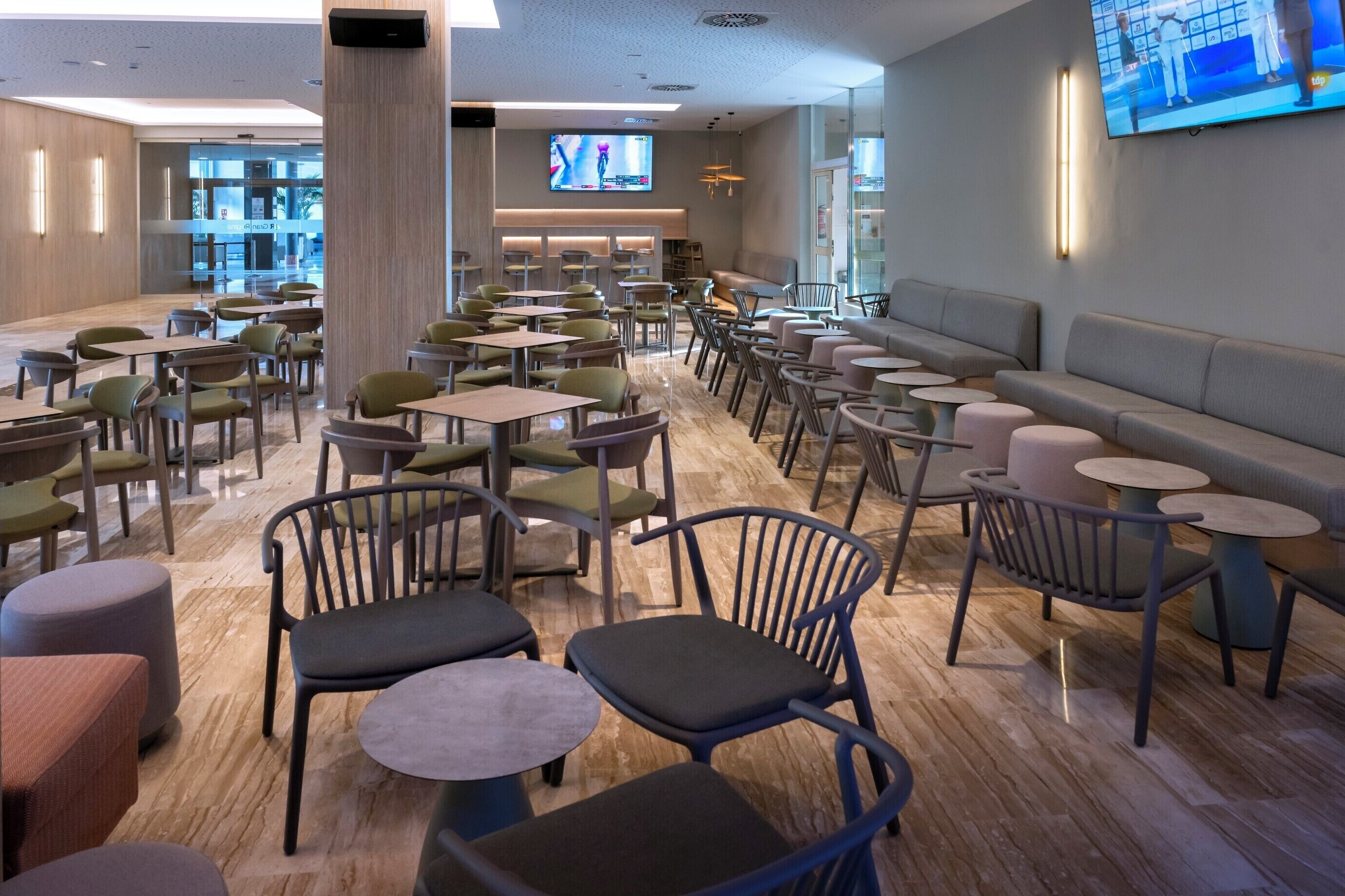 Ruime binnenruimte met diverse zithoekjes, waaronder tafels en stoelen, een groot televisiescherm en een modern interieur.