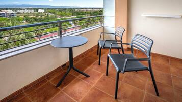 Un balcón con una mesa redonda y dos sillas, barandilla y vista panorámica de la ciudad.