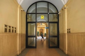 Um corredor com uma grande entrada em arco, uma placa acima da porta e uma pessoa caminhando em direção ao fim do corredor.