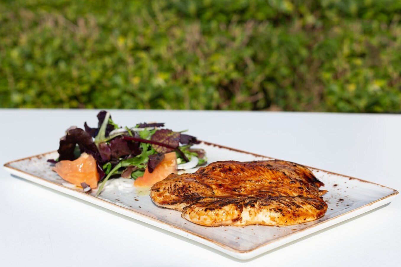 A plate with grilled chicken and a side salad on a white table.