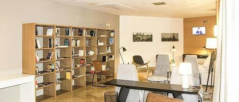 A modern hotel room with a large bookshelf, a dining area with a table and chairs, and a television on the wall.