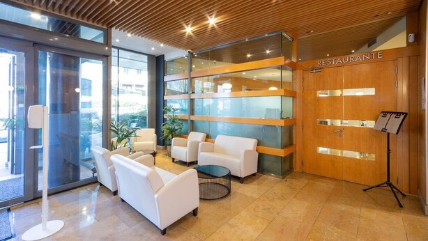 A modern lobby with a reception desk, seating area, and a 'RESTAURANTE' sign.