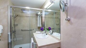 Un baño moderno con ducha envuelta en vidrio, tocador doble y un espejo grande.