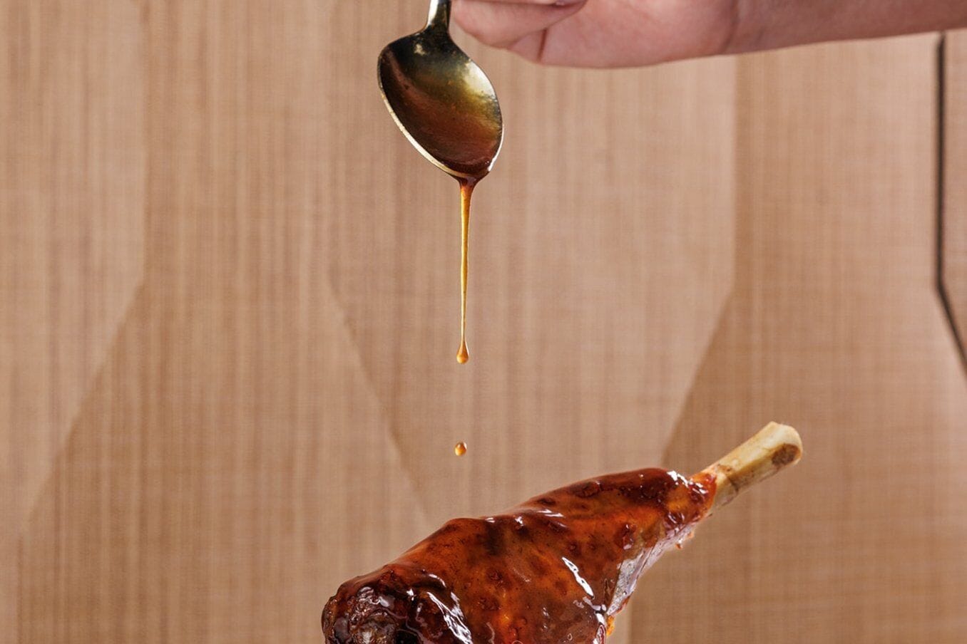 Ein Löffel, von dem Soße auf Fleisch tropft.
