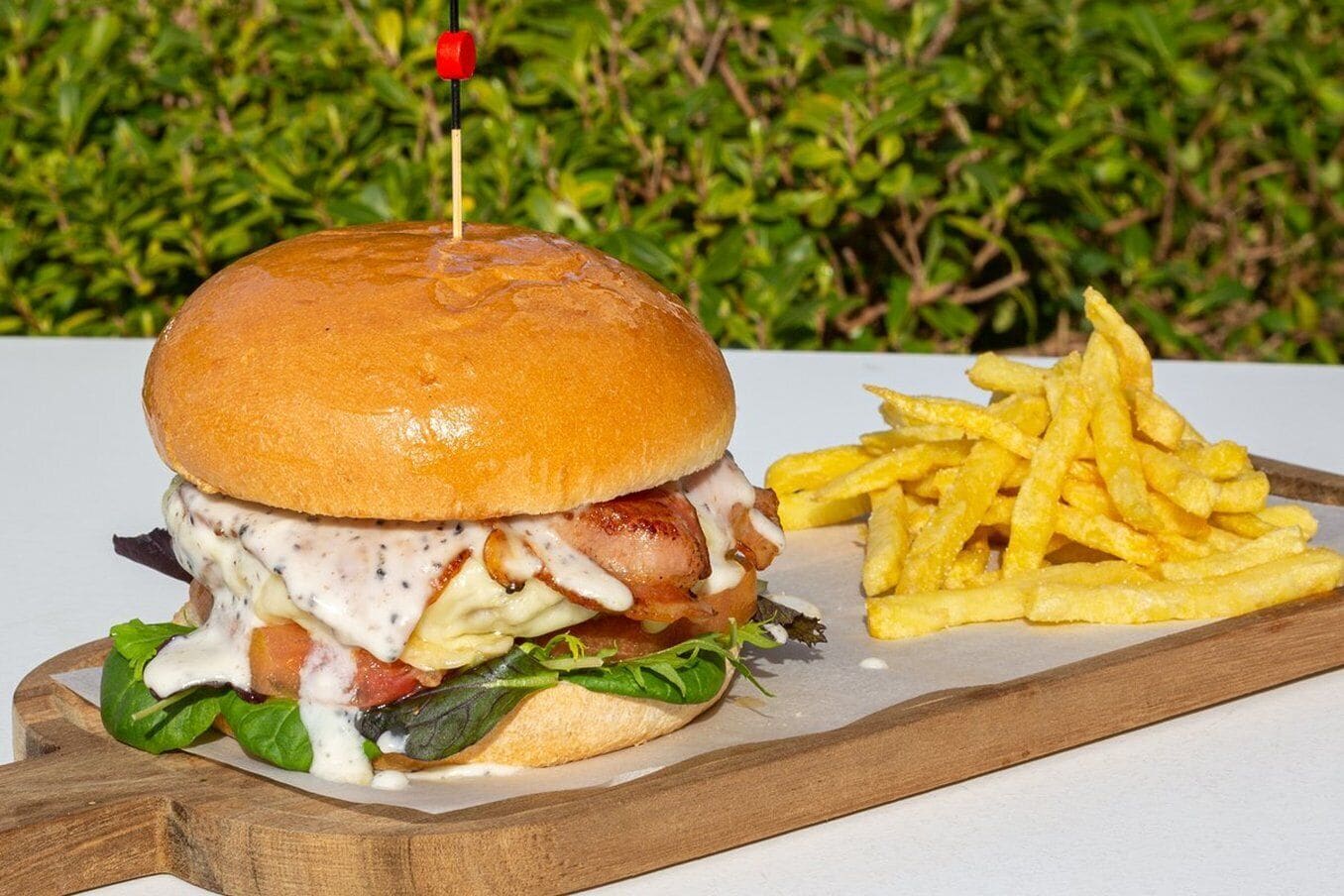 A burger with a toothpick on top, accompanied by a side of fries, served on a wooden board.
