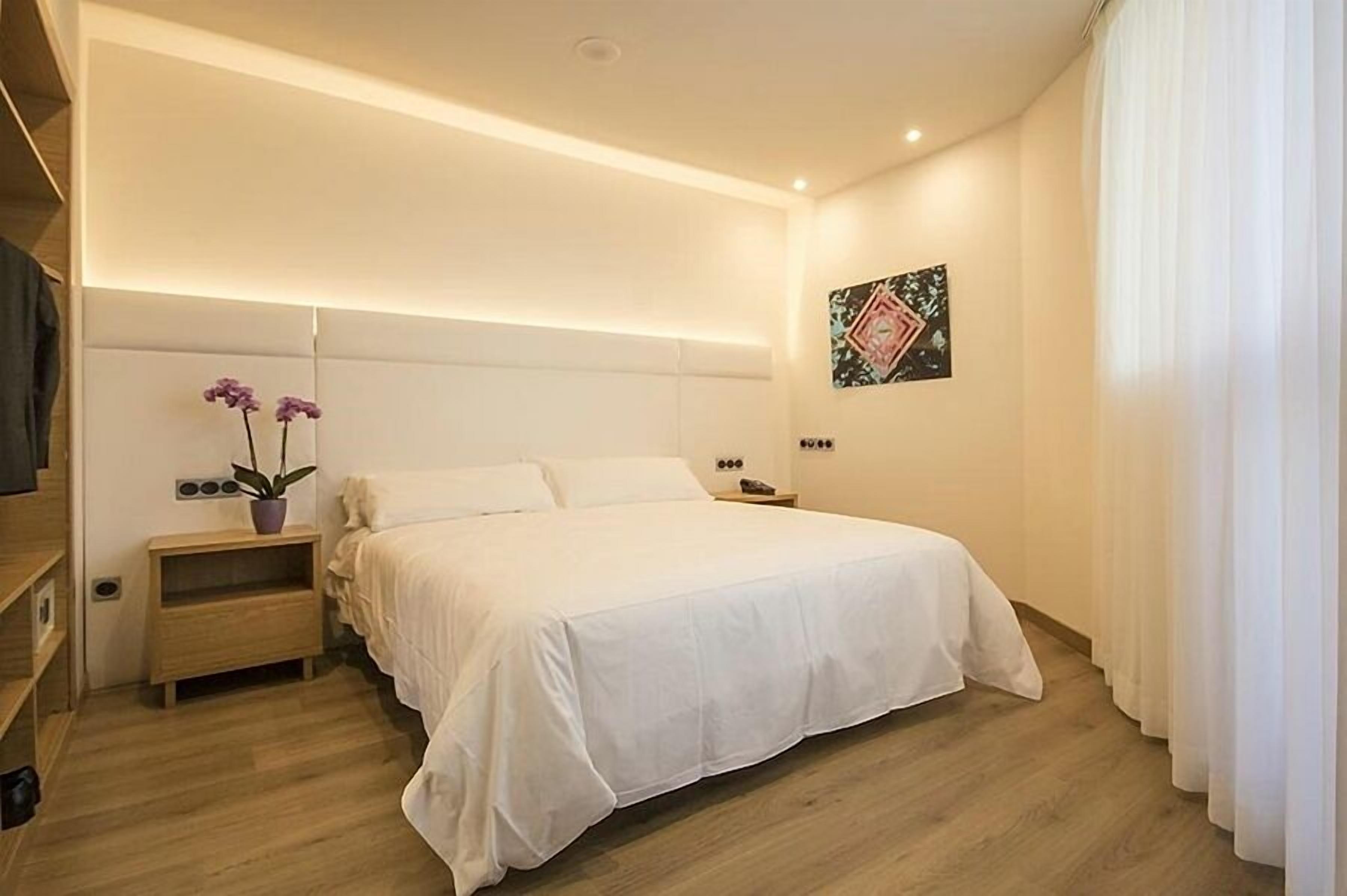 A modern bedroom with a large bed, bedside tables, a nightstand, and a wall-mounted artwork.