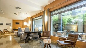 A modern hotel room with a large window, a desk, comfortable seating, and a visible outdoor garden.