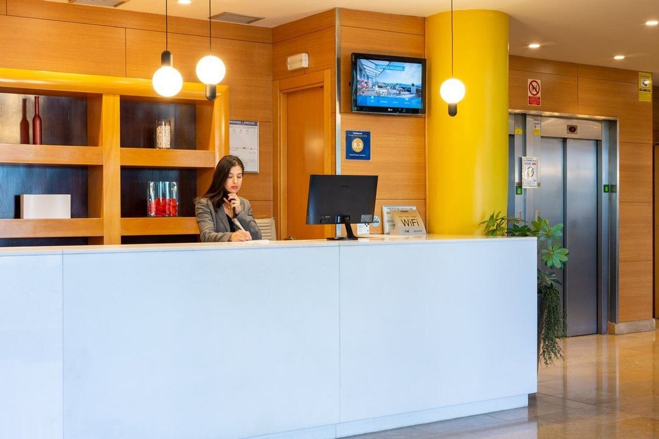 A reception desk with a computer, a television mounted on the wall, and a sign indicating WiFi availability.