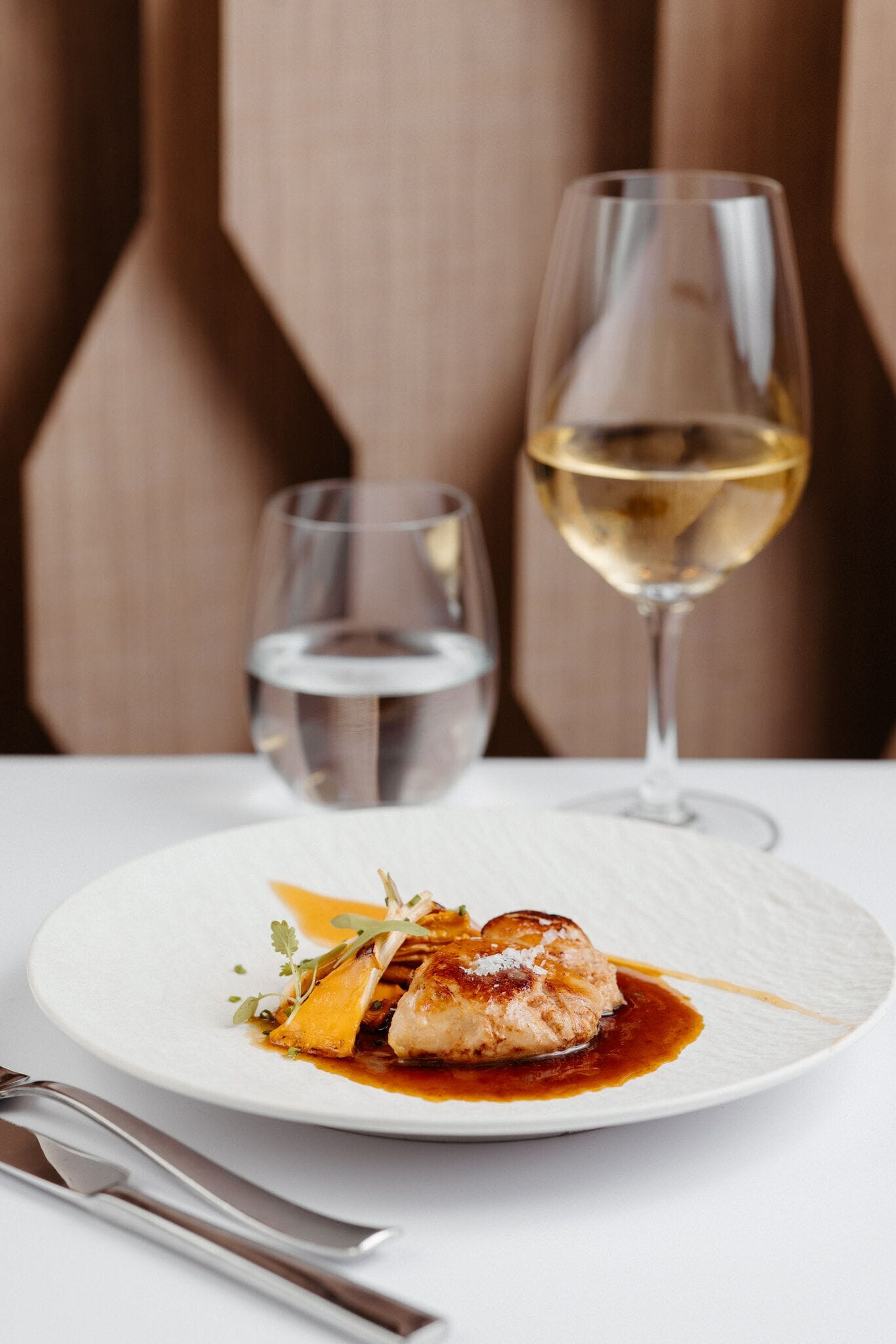 A plate of food with a glass of white wine and a glass of water on a table.