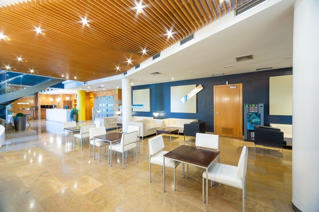 A spacious lobby with a modern design, featuring a reception area, seating arrangements, and a staircase.