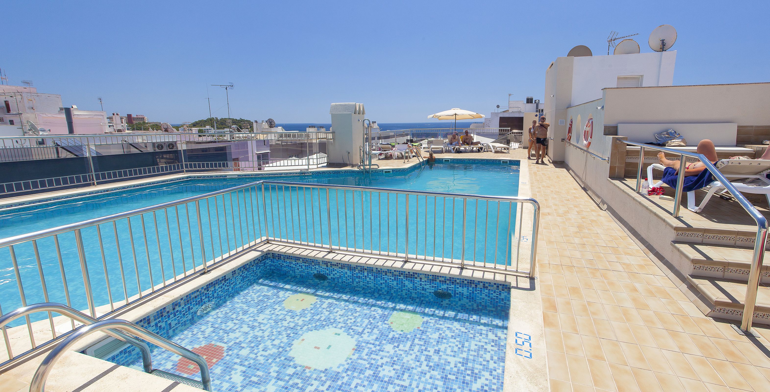 Una piscina en la azotea con vista al mar, rodeada de sillas de descanso y sombrillas.