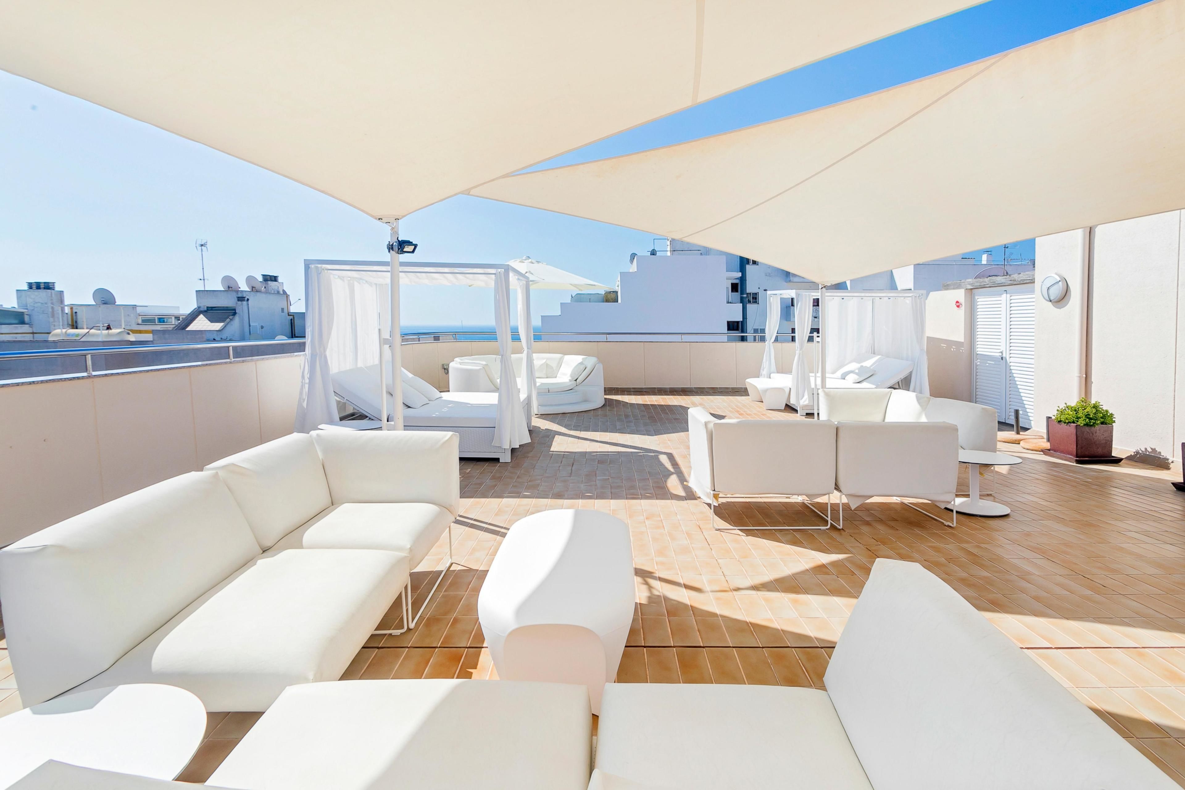 Una terraza en la azotea con sillones blancos y un toldo, con vistas al horizonte urbano.
