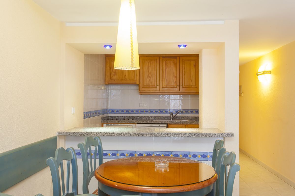 A compact kitchen with wooden cabinets, a granite countertop, and a dining area with a round table and blue chairs.