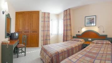 A hotel room with two beds, a desk with a telephone, a television, and a large wooden wardrobe.