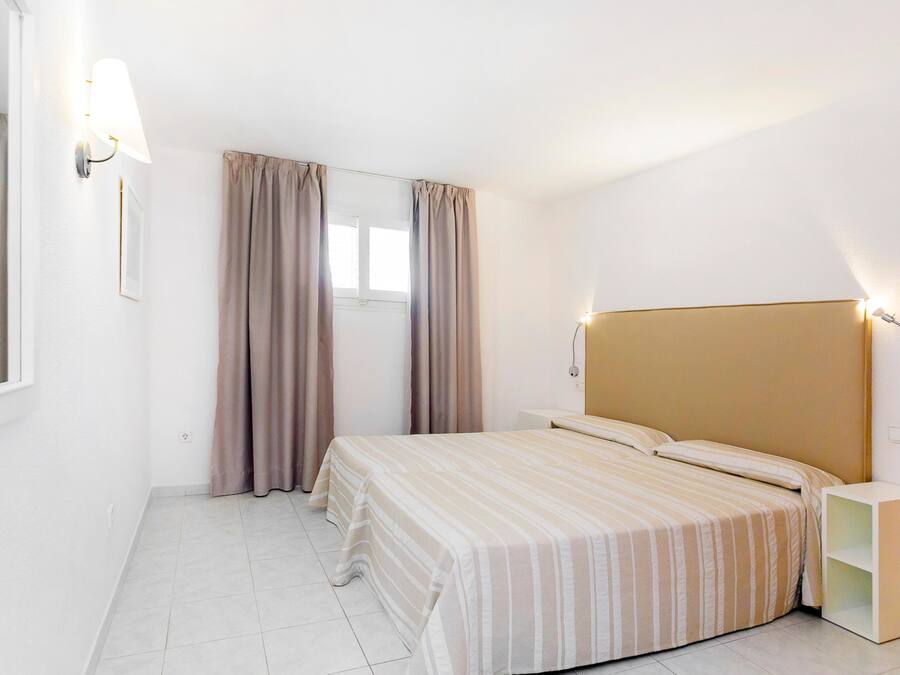 Un dormitorio con cama, cortinas, una mesita de noche y una lámpara de pared.