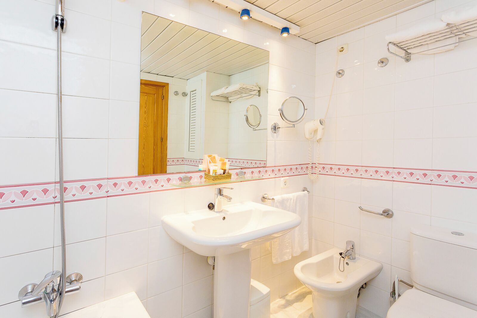 Une salle de bain équipée d’un lavabo, d’un bidet et d’une douche. Un miroir se trouve au-dessus du lavabo et un porte-serviettes est fixé au mur.