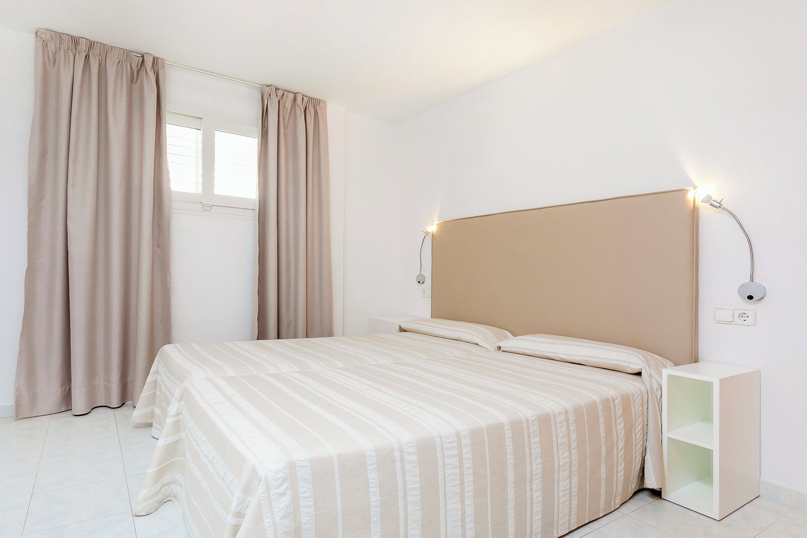A bedroom with a bed, curtains, a bedside table, and a wall-mounted light fixture.