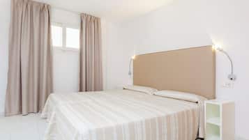 A bedroom with a bed, curtains, a bedside table, and a wall-mounted light fixture.