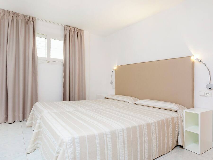 A bedroom with a bed, curtains, a bedside table, and a wall-mounted light fixture.