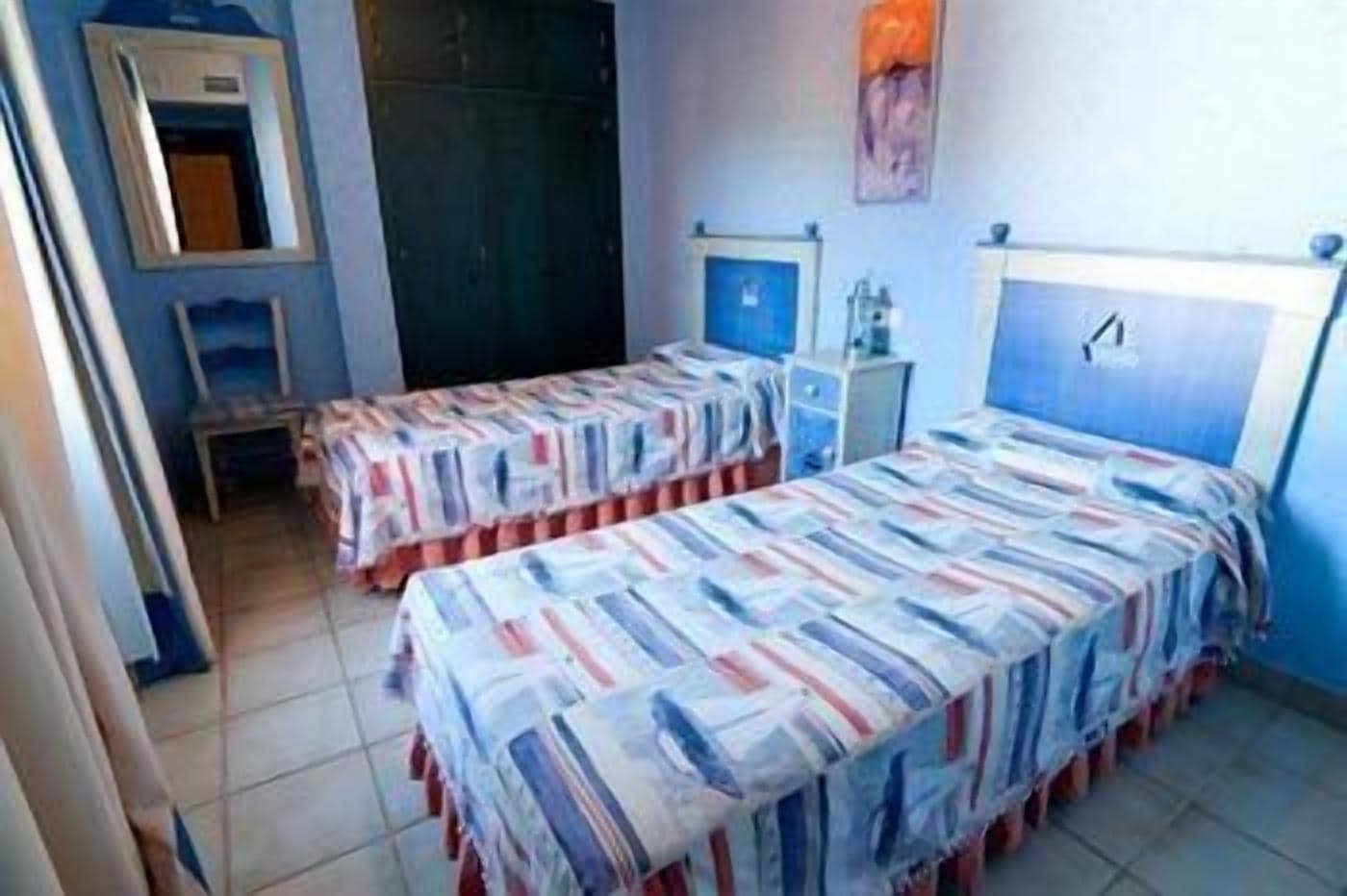 A room with two beds, a small table, a mirror, and a cabinet.