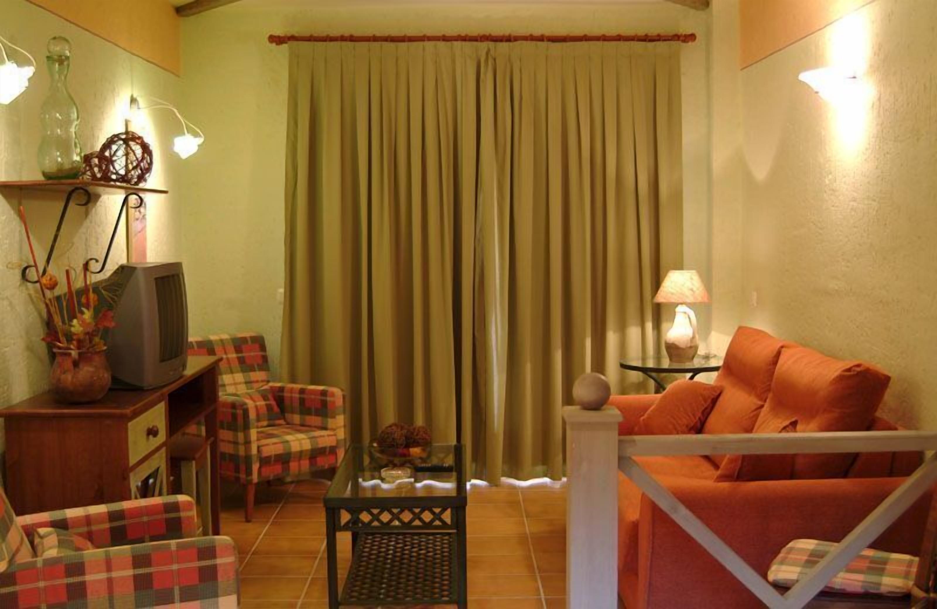 A cozy living room with a television, plaid chairs, a sofa, and a curtain.