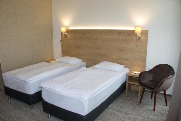 Quarto de hotel com duas camas de solteiro, cabeceira de madeira, luminárias de cabeceira, mesa de cabeceira e uma cadeira.