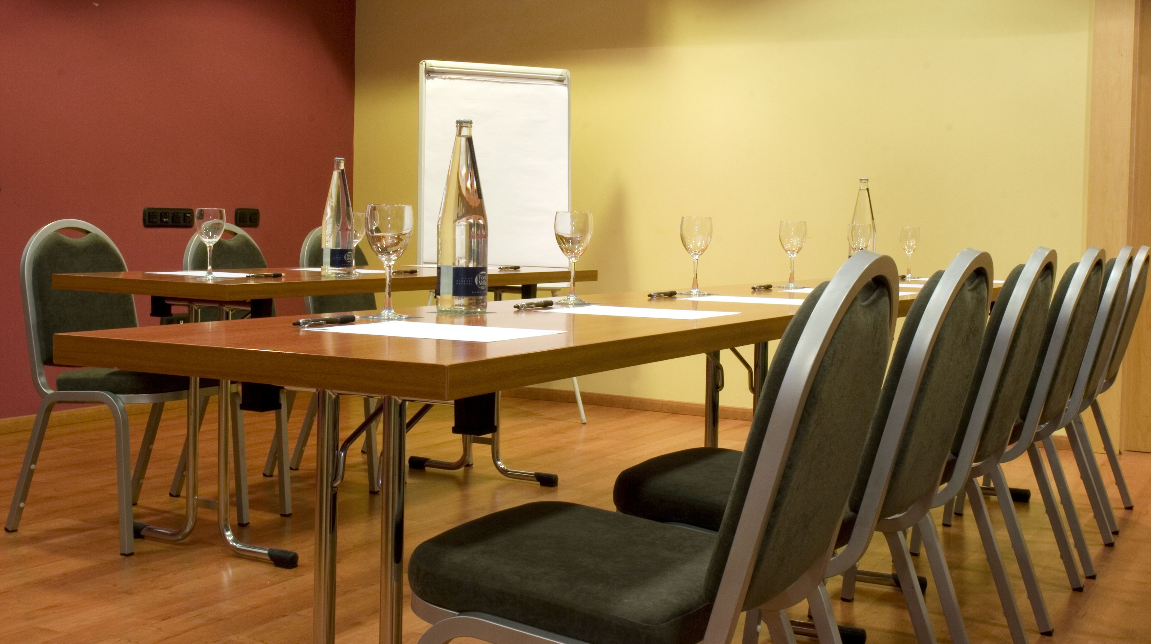 A conference room with a long table, chairs, a whiteboard, and several wine glasses.