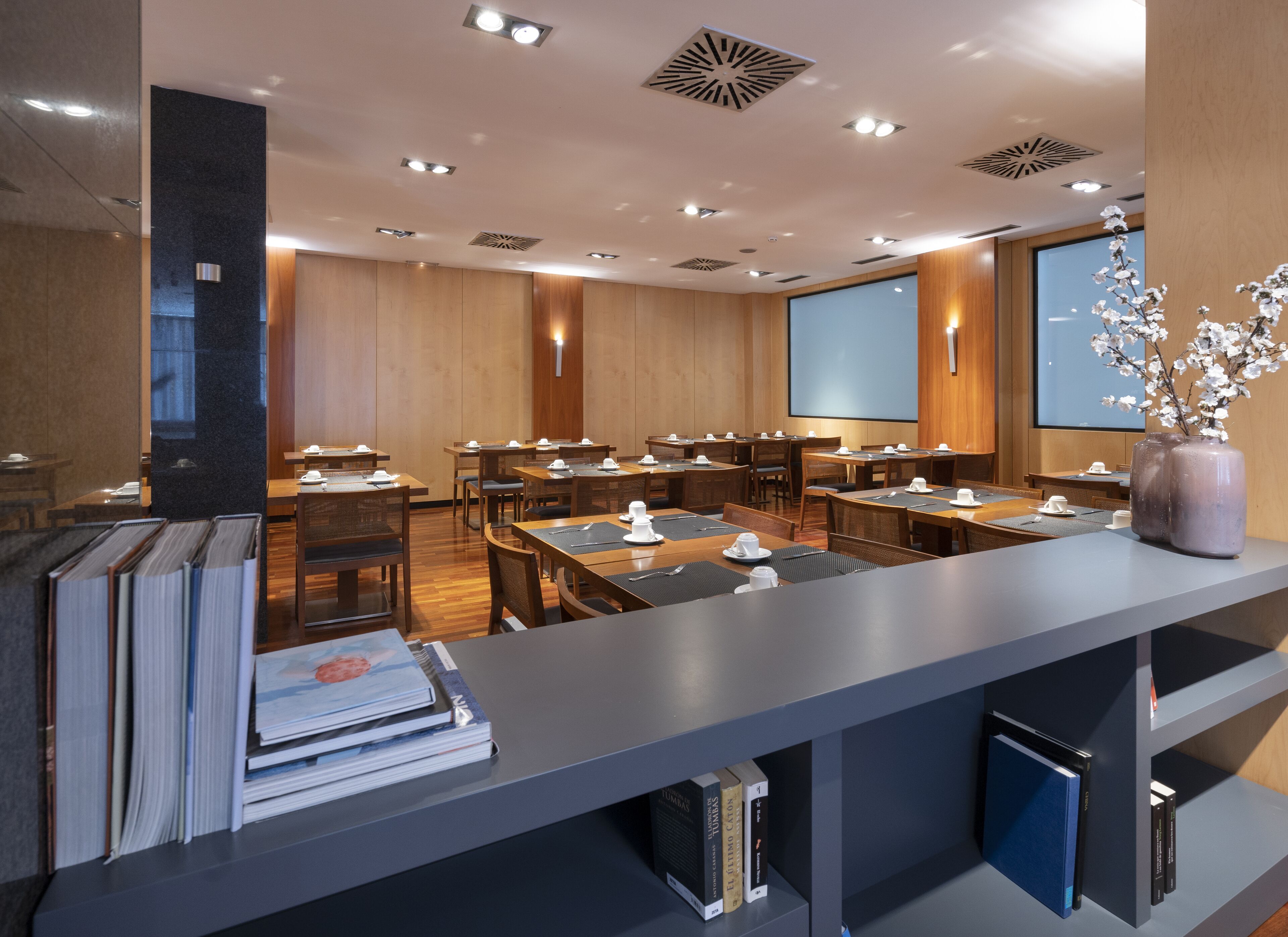 A conference room with tables set for a meeting, a projector screen, and a bookshelf with books.
