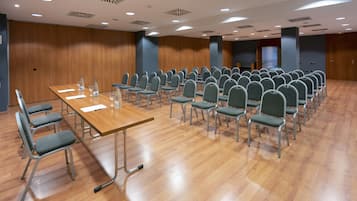 Une salle de conférence avec une longue table et des rangées de chaises, des murs en bois et des luminaires au plafond.