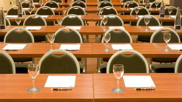 A conference room with rows of tables, each with a glass of water, a pen, and a notepad.