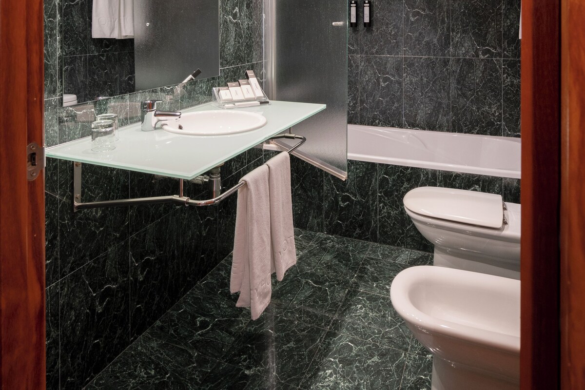 Une salle de bain moderne avec un meuble-lavabo entouré de parois en verre, une baignoire séparée et des toilettes.