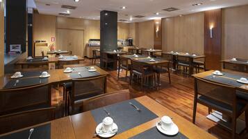 Un comedor de hotel con varias mesas y sillas, equipado con vajilla y una estación de café.