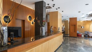 Un espace d’accueil moderne, avec un comptoir de réception en bois, un grand vase rempli de fleurs et un coin salon agrémenté de canapés rouges et gris.