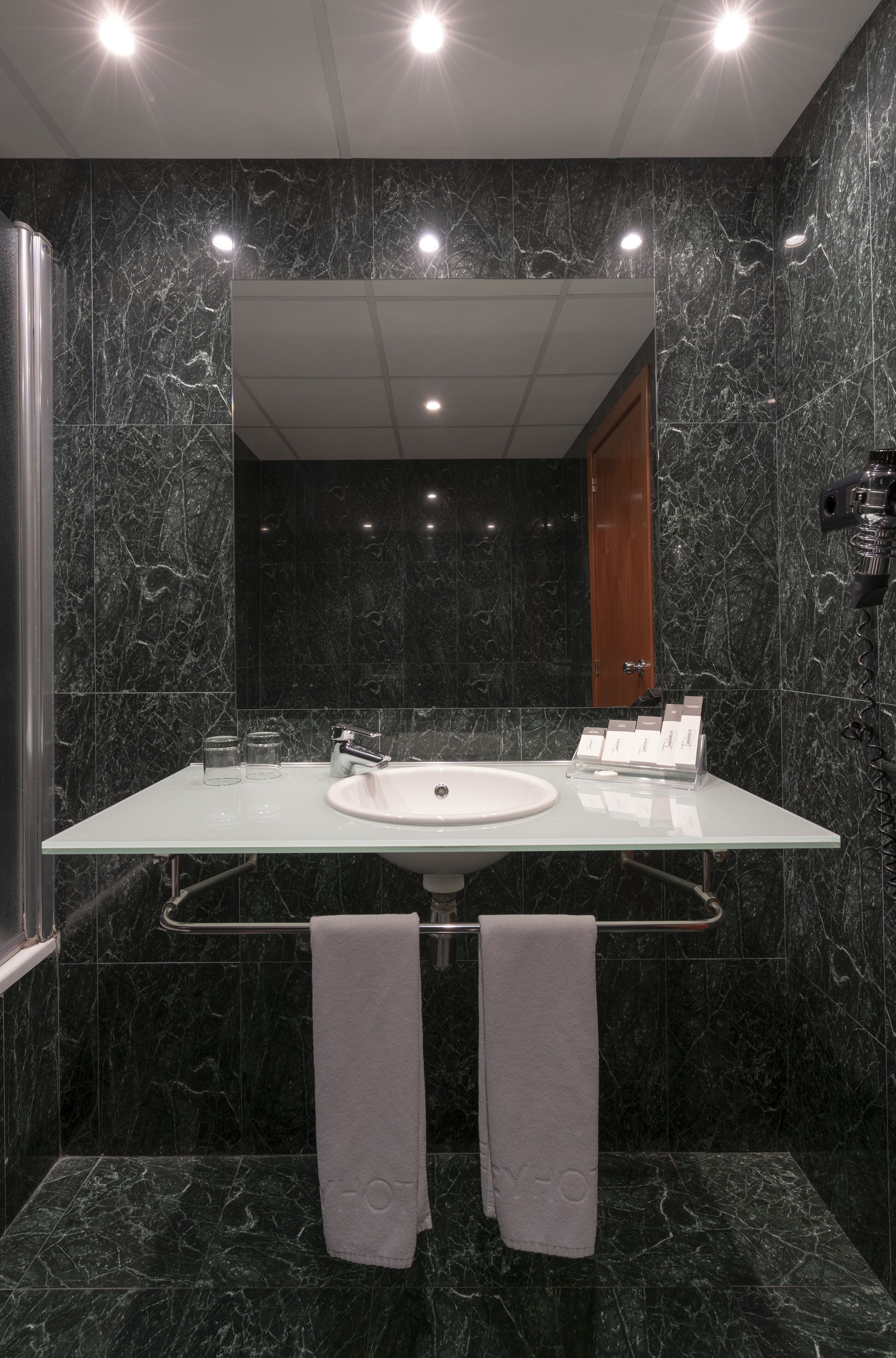Un baño moderno con un espejo grande, un lavamanos blanco y dos toallas.