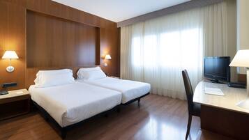 Habitación de hotel con dos camas, un escritorio con computadora y televisión.