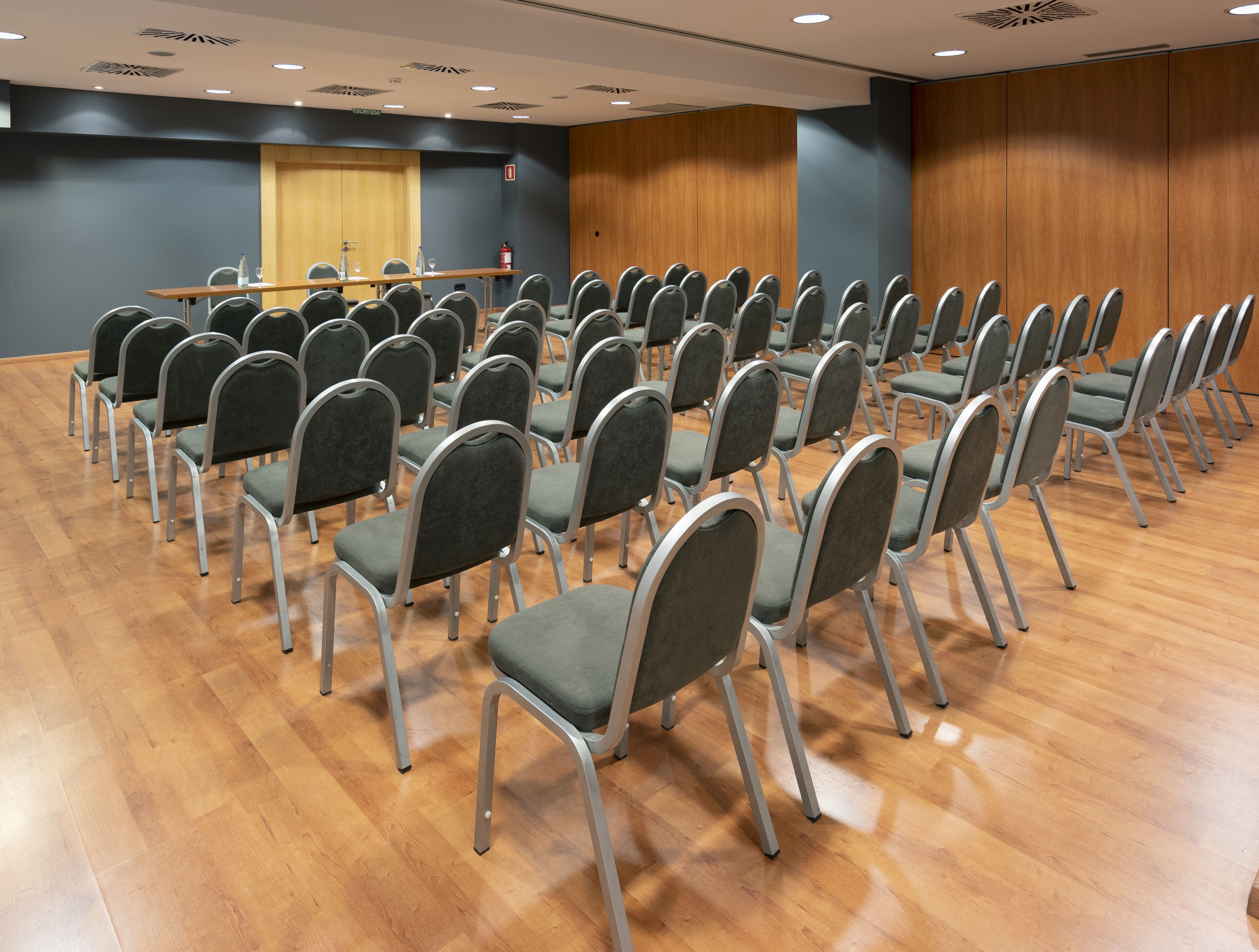 Ein Konferenzraum mit Stuhlreihen, einem Holztisch und einem Feuerlöscher.