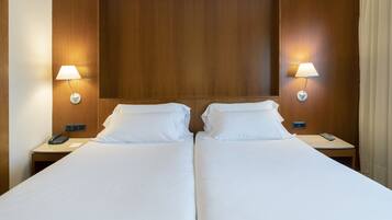 A double bed with white linens, two bedside tables with lamps, and a wooden headboard.