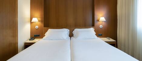 Cama doble con sábanas blancas, dos mesitas de noche con lámparas y cabecero de madera.