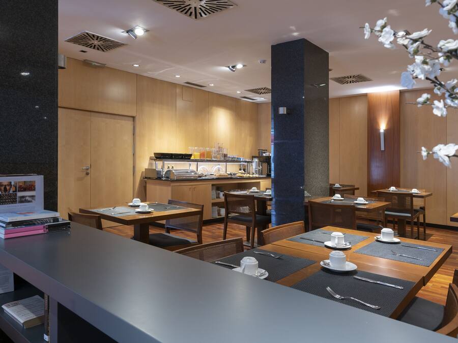 Un comedor de hotel moderno con mesas y sillas de madera, y un mostrador para buffet.