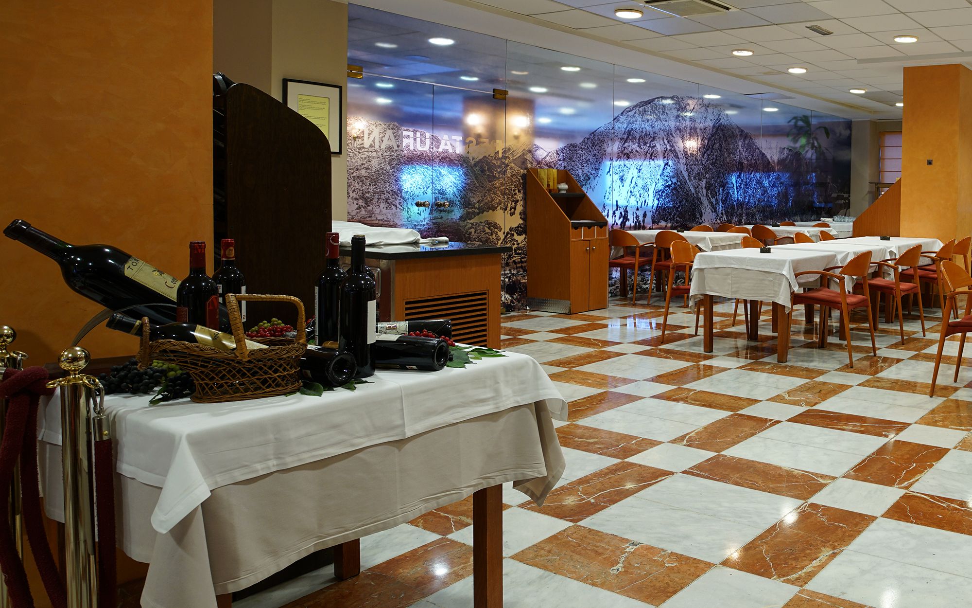 A restaurant with a checkered floor, tables with white tablecloths, and wine bottles on a table.