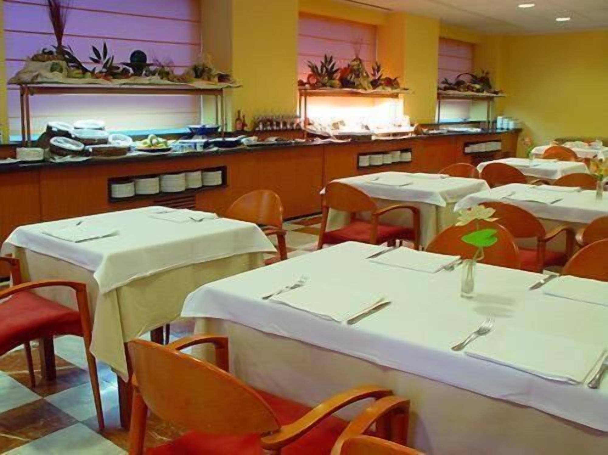 A restaurant with multiple tables, each covered with a white tablecloth and equipped with cutlery.