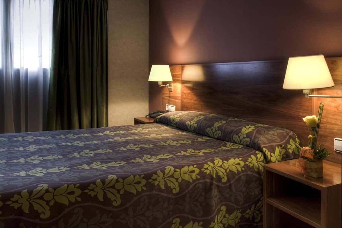 Une chambre d’hôtel avec un lit, deux lampes de chevet, une table de chevet et une fenêtre avec des rideaux.