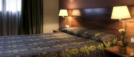 Una habitación de hotel con cama, dos lámparas de noche, una mesita de noche y una ventana con cortinas.